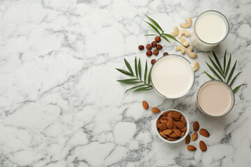 Different vegan milks and ingredients on white marble table, flat lay. Space for text