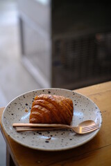 Fresh french croissant on white ceramic plate on wooden table