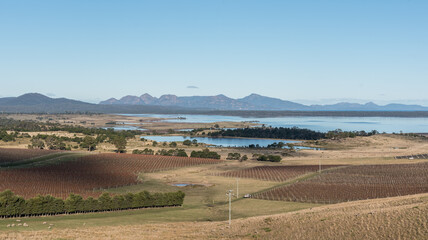 View of Great Oyster Bay in Tasmania, with farmland and vineyards in the foreground - obrazy, fototapety, plakaty