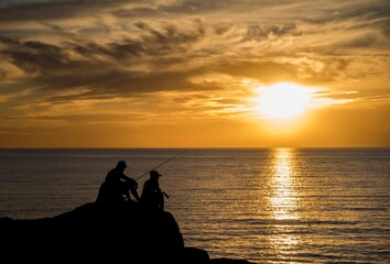 Naklejka na ściany i meble Silhouette of fishermen at sunset