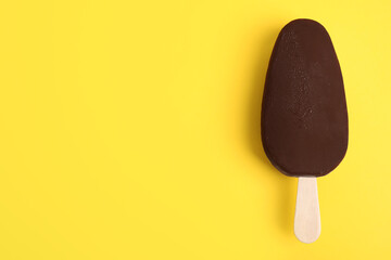 Ice cream glazed in chocolate on yellow background, top view. Space for text