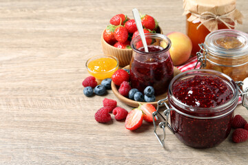Jars with different jams and fresh fruits on wooden table. Space for text