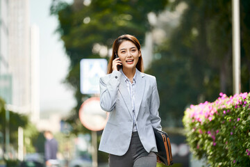 young asian business woman talking on mobile phone while walking in street