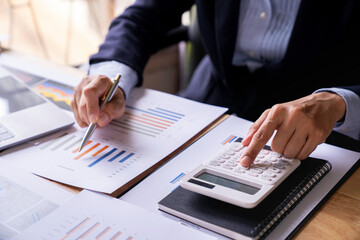 Accountant or banker working process, a Businesswoman using a calculator to calculate the numbers of statistic business profits growth rate on documents graph data, his desk in an office.