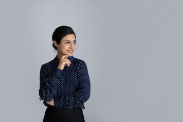 Smiling young Indian woman isolated on grey studio background look at blank empty copyspace aside thinking. Happy biracial female client consider good sale deal or promotion offer. Copy space concept.