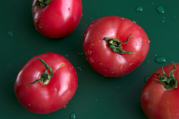 Four red ripe tomatoes on a green background.