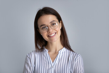 Obraz premium Headshot portrait of happy millennial Caucasian female student in glasses on grey studio background. Profile picture of smiling young businesswoman or woman client in spectacles. Employment concept.