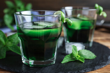 Delicious mint liqueur with green leaves on table, closeup