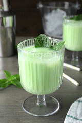 Delicious mint liqueur with ice cubes and green leaves on grey wooden table, closeup