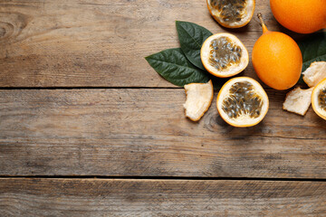 Delicious ripe granadillas and leaves on wooden table, flat lay. Space for text
