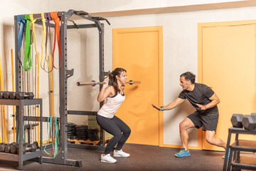 Fototapeta premium Sportswoman doing squats with bar with trainer in gym
