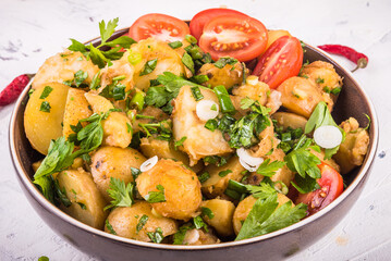 Rustic vegetarian potato salad with green onions, parsley and mint in a plate with tomato halves in a plate, close-up