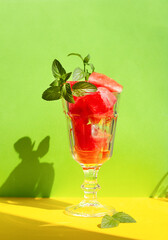 summer refreshing dessert of pieces of watermelon mixed with ice in a vintage glass on bright green and yellow background, harsh sun light and shadows