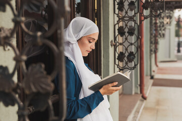 Fototapeta na wymiar Portrait of young muslim woman wearing hijab reading book outdoors