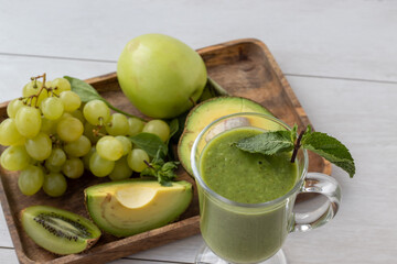 green health smoothie in a glass mug, kiwi, grapes, avocado, mint, apple on a tray Raw, vegan, vegetarian, alkaline food concept.