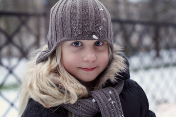 Winter portrait of happy little girl wearing knitted hat, scarf and coat