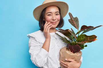 Photo of fashionable young brunette Asian woman wears white blouse and hat carried potted...