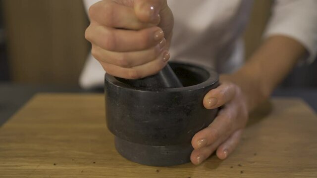 women's hands are grinding coffee beans. grinding roasted coffee manually with pestle and mortar. Close up shot of pestle blending fresh roasted coffee beans in mortar 4k footage