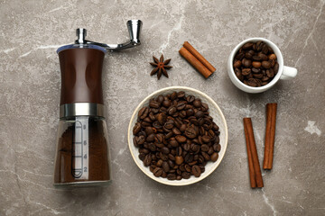 Manual coffee grinder with powder, beans and cinnamon on grey table, flat lay