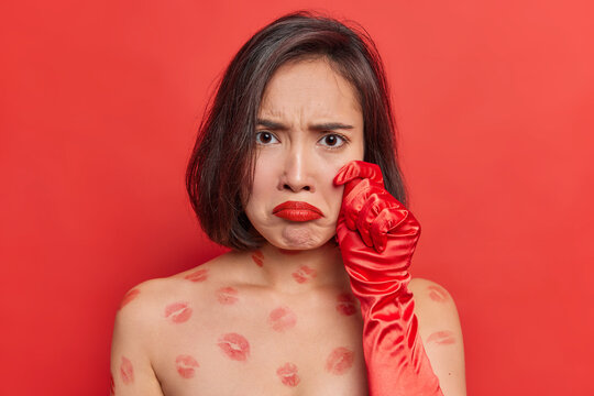 Frustrated unhappy young Asian woman purses red lips being dissatisfied with something looks gloomy at camera stands shirtless indoor against vivid backgound. Negative human facial expressions