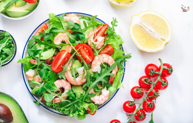 Shrimp salad with cherry tomatoes, arugula, avocado, and oil lemon dressing on white background. Top view