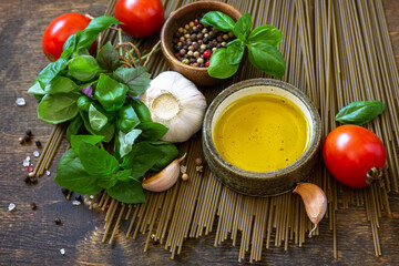 Ingredients for italy cuisine. Spinach spaghetti, herbs, spices, olive oil and tomatoes on a rustic table.