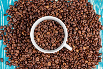 Scattered on the table beans of roasted coffee in a white cup. Morning. Cheerfulness