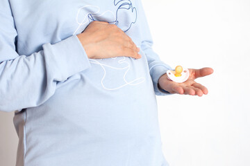 Close up of pregnant who holds a pink pacifier for a baby. Waiting. Happiness. White background, space for text.