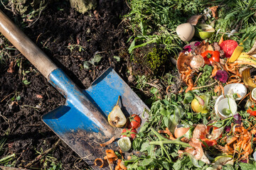 Compost box outdoors full with garden browns and greens and food  wastes, blue shovel in the soil,...