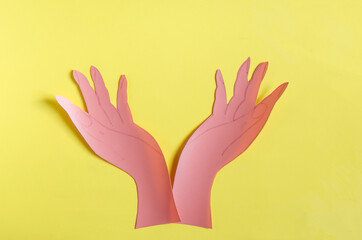Two palms made of red paper on a bright yellow background of kopi space. The concept symbol consists of two hands holding an empty space a bright background
