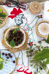 Fresh cherries in plate on embroidered tablecloth with girl holding cherries in nature, still life concept