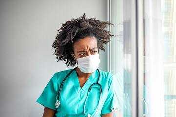 Worried nurse having a headache while working at the hospital during corona virus pandemic. Worried female doctor looking through the hospital window. The risk of frontline worker stress is real