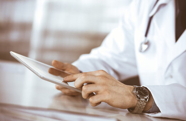 Fototapeta premium Unknown male doctor sitting and working with tablet computer in clinic at his working place, close-up. Young physician at work. Perfect medical service, medicine concept