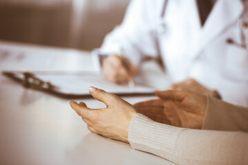 Obraz premium Unknown male doctor and patient woman discussing something while sitting in clinic and using clipboard. Best medical service in hospital, medicine, pandemic stop