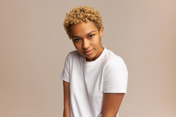 Charming African American woman with blonde Afro hairstyle standing against pale pink copy space...