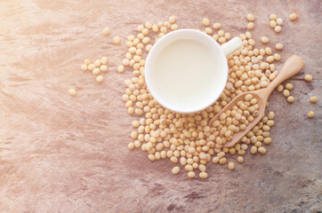 Top view of fresh delicious homemade soybean milk in soft yellow cup with dry soybean seeds on grunge background under morning sun light