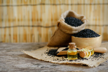 Closed up dry organic black sesame seed oil in glass bottle over some seeds in wooden bowl and sack on wooden background