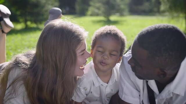 Multiracial family in the park. Mom and Dad kiss their mestizo son.