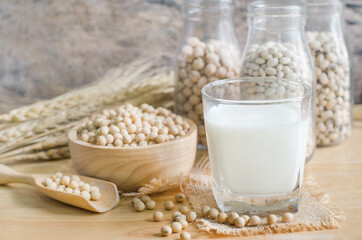 Closed up fresh organic soybean milk in glass bottle with fresh seeds on wooden background in soft light tone