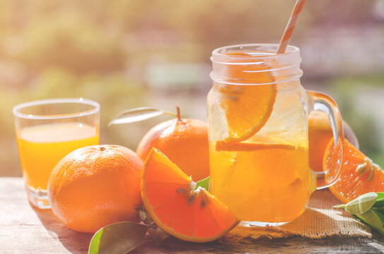 Fresh orange juice in glass and some fruit on grunge background on table under warm sun light in morning time