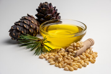 Pine nuts oil with peeled pine nuts and pine cones on white background