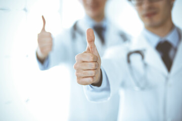 Two male doctors standing as a team and showing thumbs up as a symbol of the best service for patients in the clinic. Medicine and health care