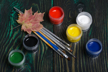 Gouache set for school. Tins of paint lie on pine boards. Nearby are paintbrushes and autumn maple...