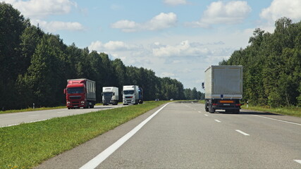 Two European semi trucks on suburban highway with grassy safety lane at Sunny summer day on blue cloudy sky background, beautiful road landscape