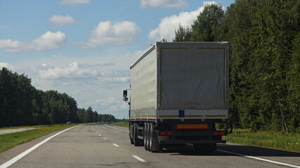 One European awning van semi truck back side closeup view drive on the suburban highway road at Sunny summer day on blue sky with white clouds background, cargo trucking transportation logistics