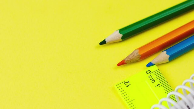 multicolored sharp wooden colored pencils lie on a pastel yellow background with a ruler, slow motion 4k. Concept for school