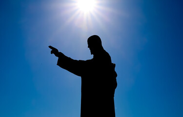 View on silhouette of jesus christ statue against blue sky background with raised arm, sun star...