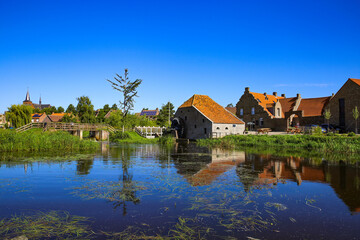 Fototapeta na wymiar View over reflecting river pond on old water mill restaurant against deep blue cloudless summer sky - Neer (Limburg), Netherlands