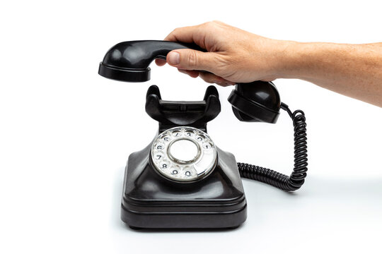 MALE HAND LIFTING OLD ROTARY DIAL BLACK PHONE ISOLATED ON WHITE BACKGROUND.