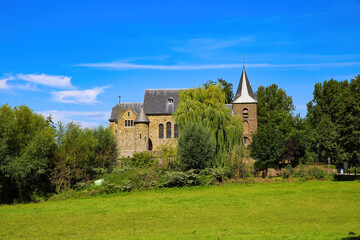 View on medieval church and fortress in rural dutch landscape with green trees against blu summer sky - Sint Dionysiuskerk in Asselt near Roermond, Netherlands